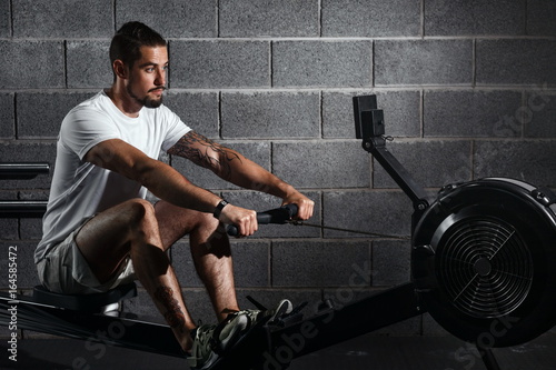 Bild auf Leinwand Fitness young man using rowing machine in the gym