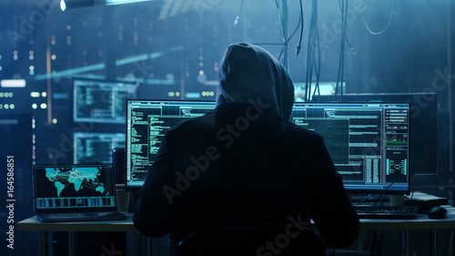 Dangerous Hooded Hacker Breaks into Government Data Servers and Infects Their System with a  Virus. His Hideout Place has Dark Atmosphere, Multiple Displays, Cables Everywhere. photo