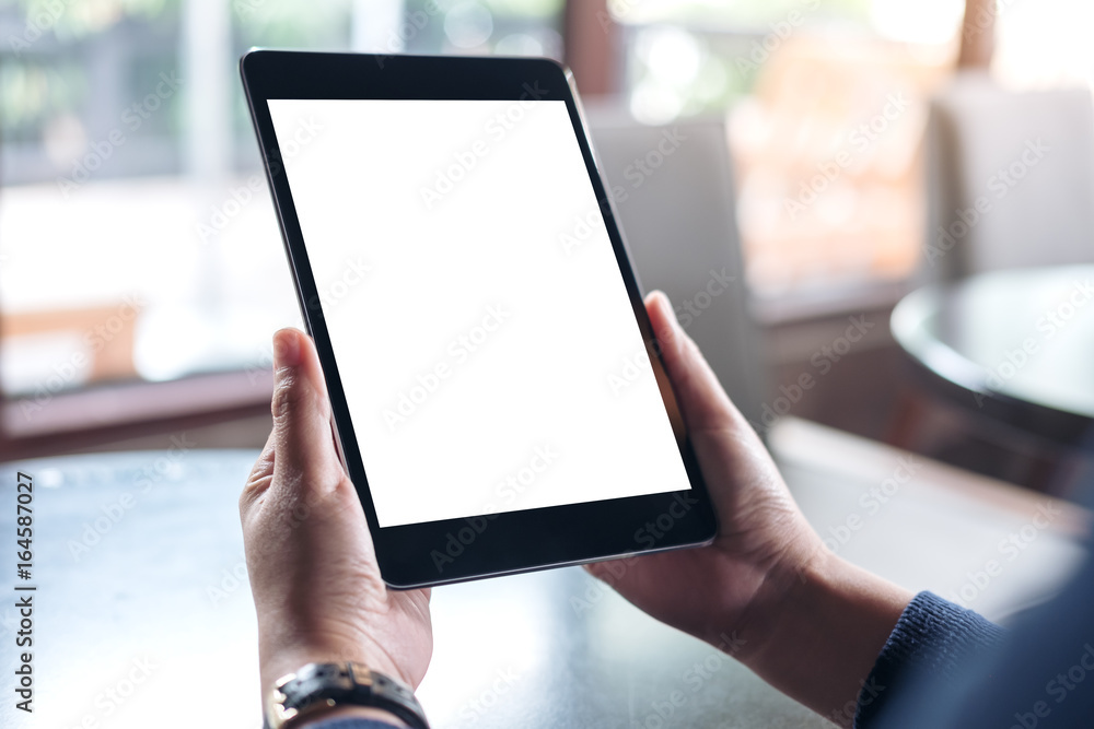 Fototapeta premium Mockup image of hands holding black tablet pc with white blank screen in modern cafe