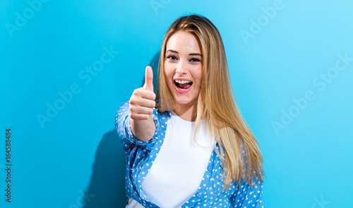 Happy young woman giving a thumb up on a blue background