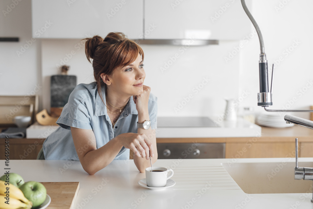 Pretty ginger Caucasian woman standing at kitchen and enjoying morning coffee. Pretty ginger Caucasian woman standing at kitchen and enjoying morning coffee.