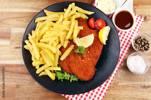 Dish of Wiener schnitzel and French fries served with sauces and salad on rustic wooden table