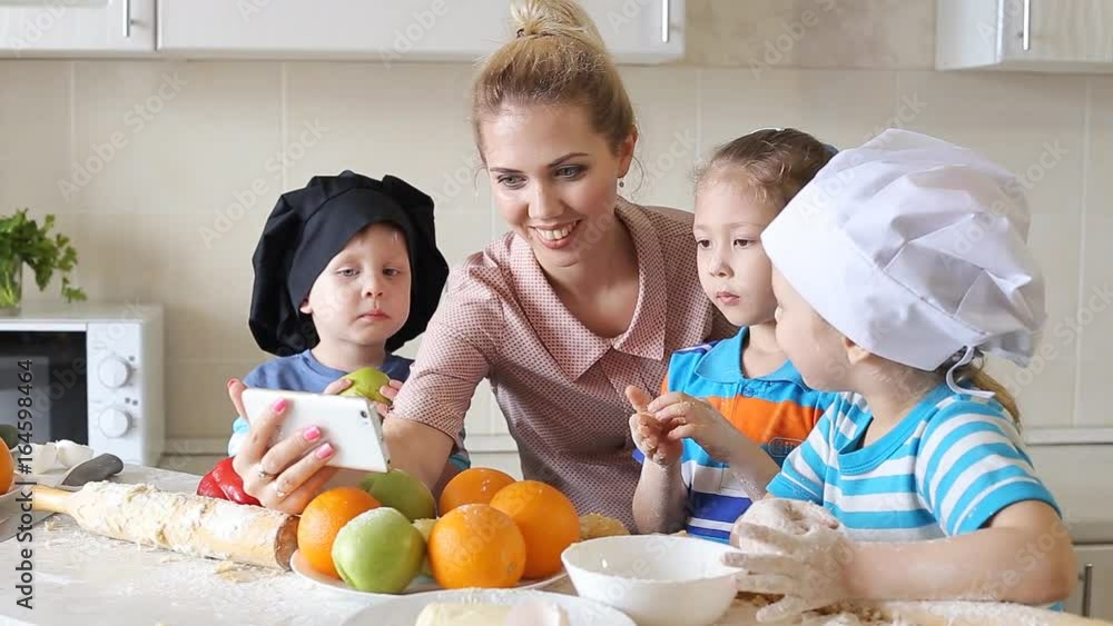Mother shows children how to cook. Girl looking a recipe on a mobile phone. Mother shows children how to cook. Girl looking a recipe on a mobile phone.