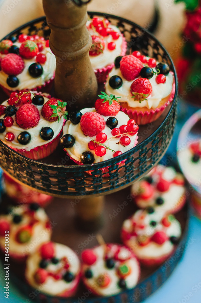 Muffins with cream and berries lie on a two-level stand in the zone of the wedding banquet.