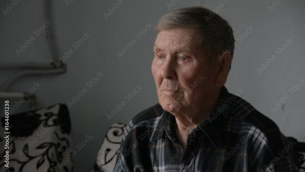 Old grandfather looking thoughtfully aside sits on the couch in the interior of a village apartment Old grandfather looking thoughtfully aside sits on the couch in the interior of a village apartment