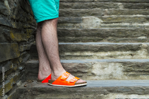 Young man's legs with neon orange slippers standing on stone stairs