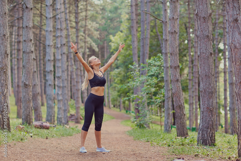 The sports girl raised her hands in the forest. 