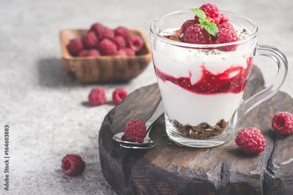 Raspberry layer dessert or breakfast with natural yogurt in a glass mug and ripe raspberries
