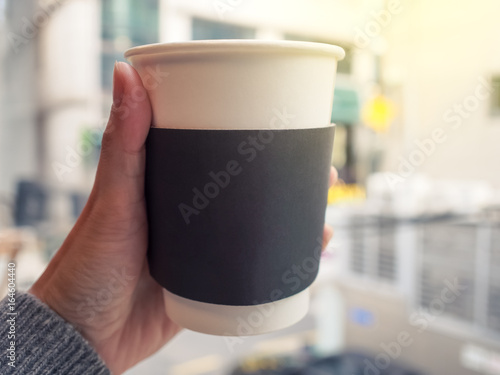 Female hand holding a paper cup of hot coffee, selective focus.