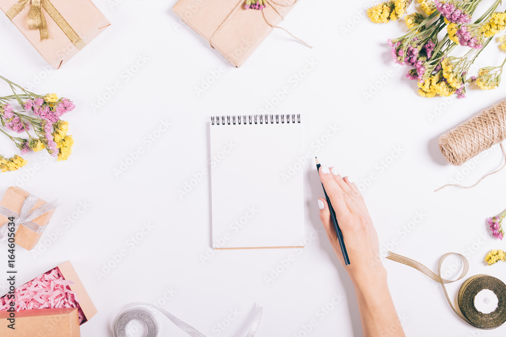 Female hand writing in a paper notebook on a white table with decorations Female hand writing in a paper notebook on a white table with decorations
