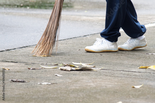 Student sweeping dried leafs on the floor in school.