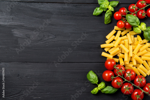 Food ingredients for Italian tortiglioni pasta with cherry tomatoes and basil leaves, black wooden background, top view with copy space