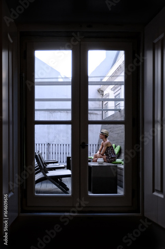 Chica sentada pensando en un patio interior vista a través de la ventana photo