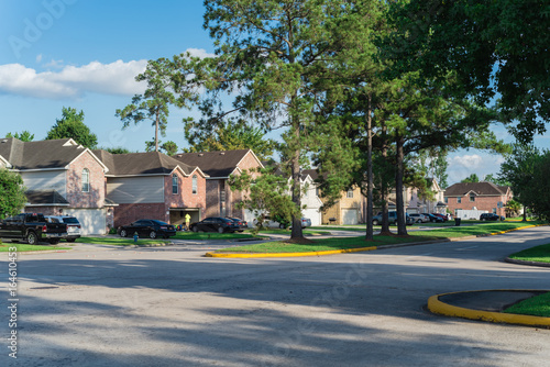 Suburban residential street with row of modern townhomes in Humble, Texas, US. Red brick houses surrounded with tall pine trees and cloud blue sky. Corner view of multi-story townhouses development. photo