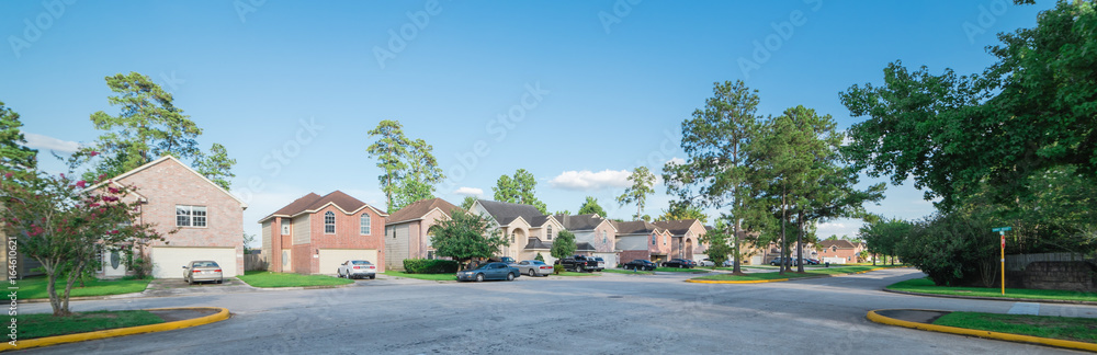 Suburban residential area, row of modern townhomes in Humble, Texas, US. Red brick houses surrounded with tall pine trees, cloud blue sky. Panorama view street intersection and multi-story townhouses. - obrazy, fototapety, plakaty 