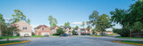 Suburban residential area, row of modern townhomes in Humble, Texas, US. Red brick houses surrounded with tall pine trees, cloud blue sky. Panorama view street intersection and multi-story townhouses.