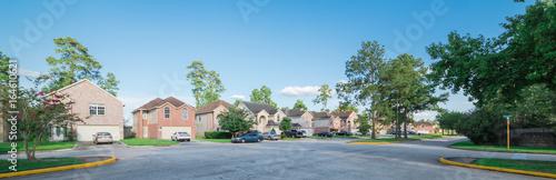 Suburban residential area, row of modern townhomes in Humble, Texas, US. Red brick houses surrounded with tall pine trees, cloud blue sky. Panorama view street intersection and multi-story townhouses. photo