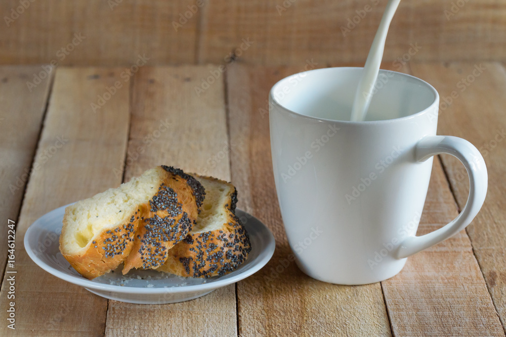Crackers with poppy seeds on a plate. Milk is poured into a white mug.Wooden table. Crackers with poppy seeds on a plate. Milk is poured into a white mug.Wooden table.