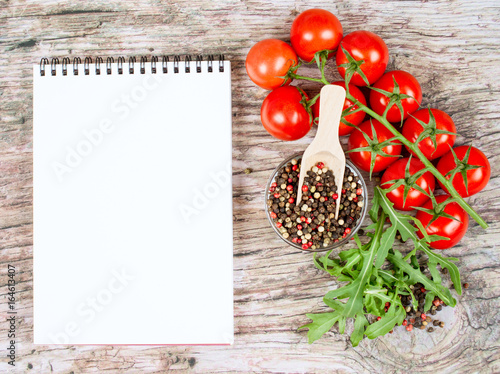 Horizontal food banner with cherry tomatoes, arugula, peppercorns and notebook on wooden background. Empty space for text.