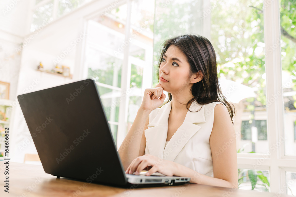 Portrait of happy beautiful young confident Asian woman thinking while working with laptop indoor Portrait of happy beautiful young confident Asian woman thinking while working with laptop indoor