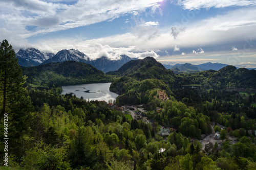 Panorama of the Alpsee lake and its forest, under a partially cloudy sky, with the romantic medieval-style castle of Hohenschwangau, in Bavaria, Germany.