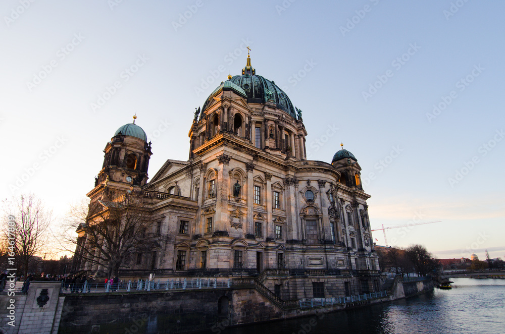 The main church Berliner Dom (Berlin, Germany), a landmark, is lit at sunrise, viewed from across the Spree river.