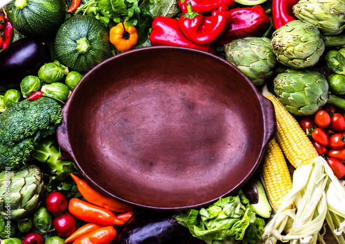 Cooking background concept. Fresh organic vegetables around empty clay pot