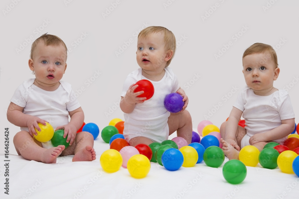 Funny baby triplets smiliing and playing with colorful balls. Studio shot Funny baby triplets smiliing and playing with colorful balls. Studio shot