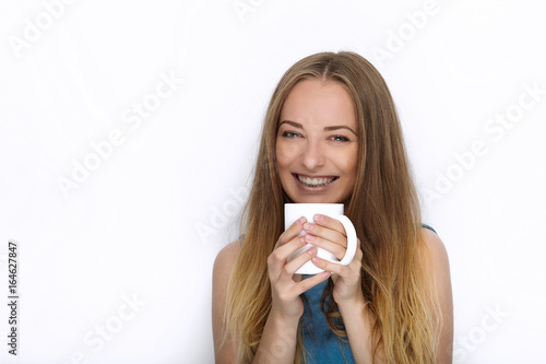 Headshot of young adorable playful blonde woman with cute smile in cobalt color blouse posing with big pure white mug on white backdrop