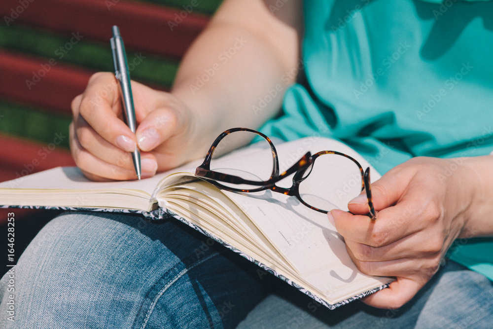 girls hands with pen writing on notebook in park girls hands with pen writing on notebook in park