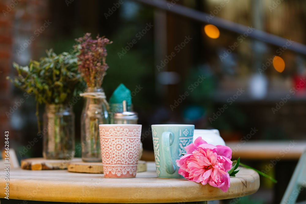 cups of tea and peony on wooden table in street cafe
