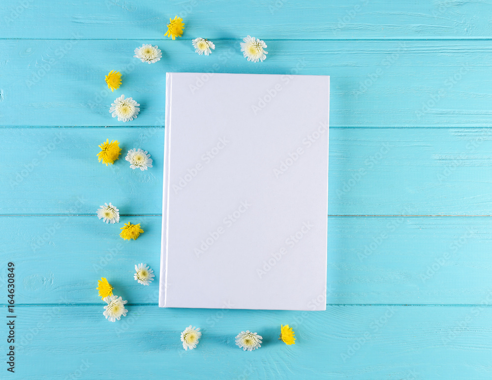 Fototapeta premium Book with blank white cover and beautiful flowers on color wooden background