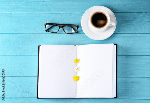 Open book with blank pages, cup of coffee and glasses on color wooden background