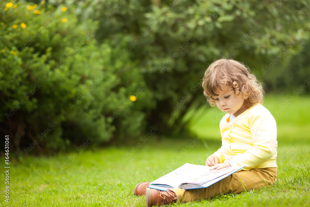 Cute toddler girl reading a book outdoors Cute toddler girl reading a book outdoors