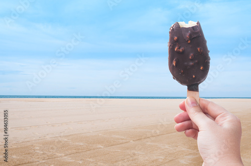 Canvas Print Woman hand holding chocolate ice cream in the summer at the beach, during the ho