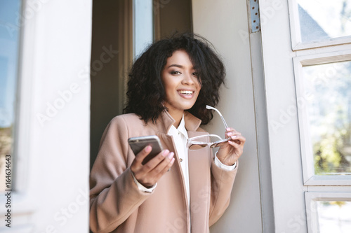 Canvastavla Pretty African American girl standing with cellphone and sunglasses in hands