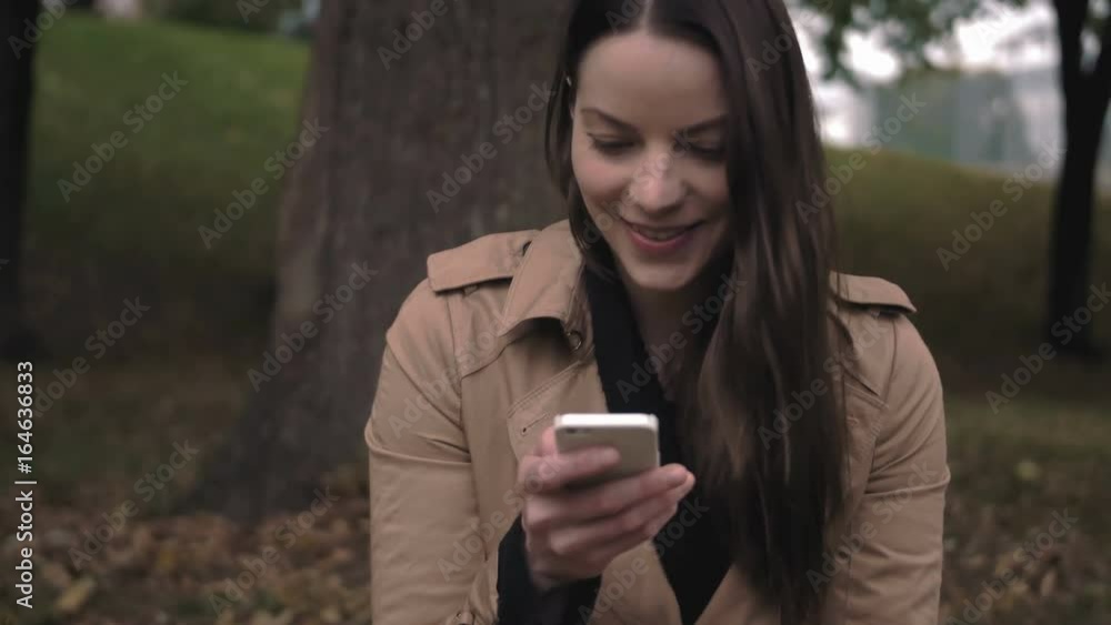 Happy young woman using her mobile device outside in the fall. Happy young woman using her mobile device outside in the fall.