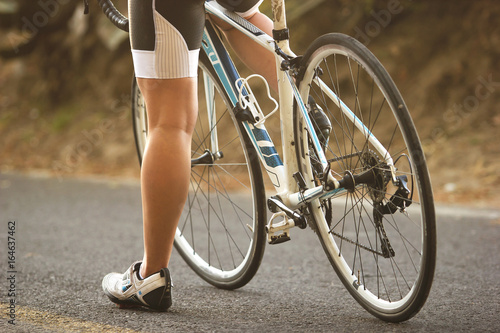 A close up to the legs of a female cyclist sitting on her road bike during sunset_