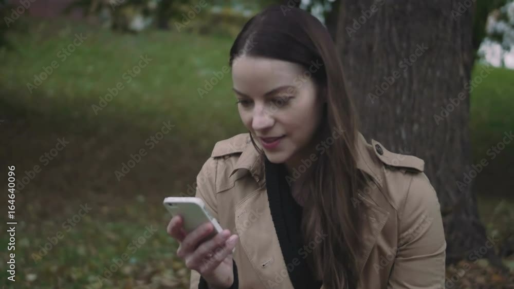 Happy young woman using her mobile device outside in the fall. Happy young woman using her mobile device outside in the fall.
