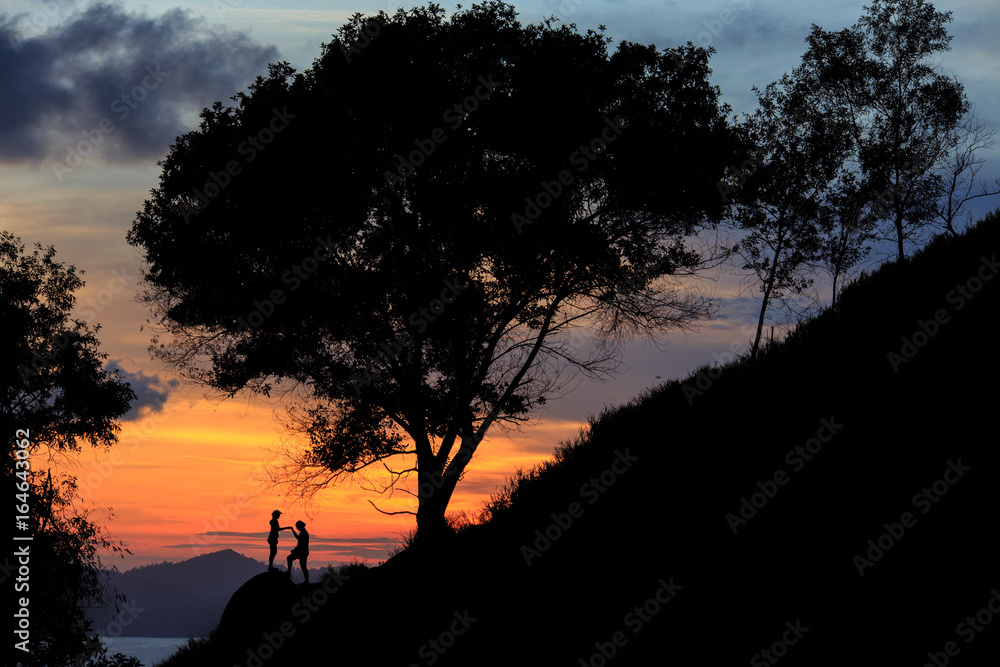 A silhouette Unidentified people standing on the rock with Beautiful sunset and silhouette tree