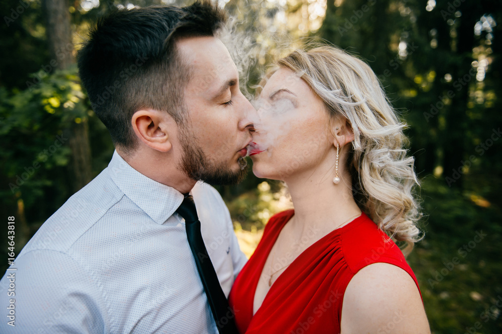 Closeup of couple of lovers kissing with smoke outdoor. Businessman and  young blonde girl with red