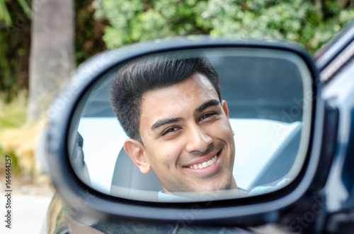 Young man sitting in a car, seen in the rear-view mirror, smiling  © mdurson