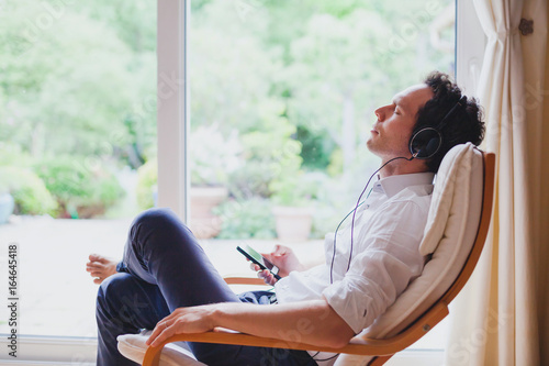 Vászonkép listening relaxing music at home, relaxed man in headphones sitting in deck chai