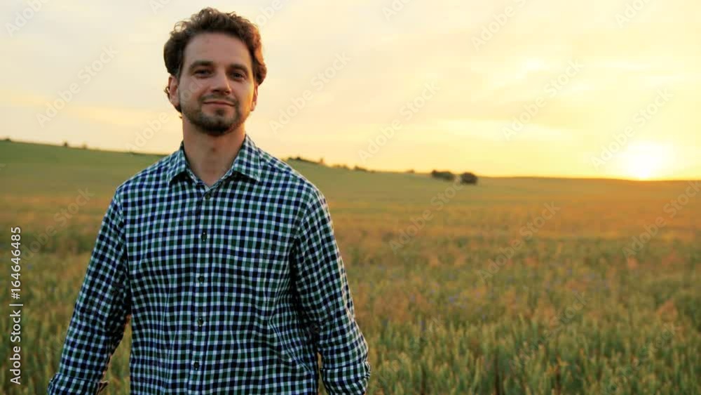 Close up portrait of smiling manwalking through the green wheat field on sunset and looking at the camera. Close up portrait of smiling manwalking through the green wheat field on sunset and looking at the camera.
