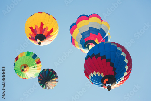 Multi colored hot air balloons flying up, group of balloons in sunny blue sky photographed from below