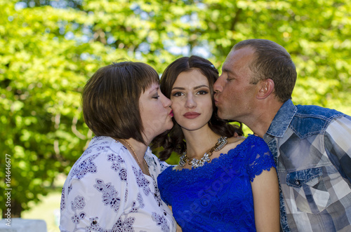 Parents kiss their adult daughter in both cheeks. © ket167600