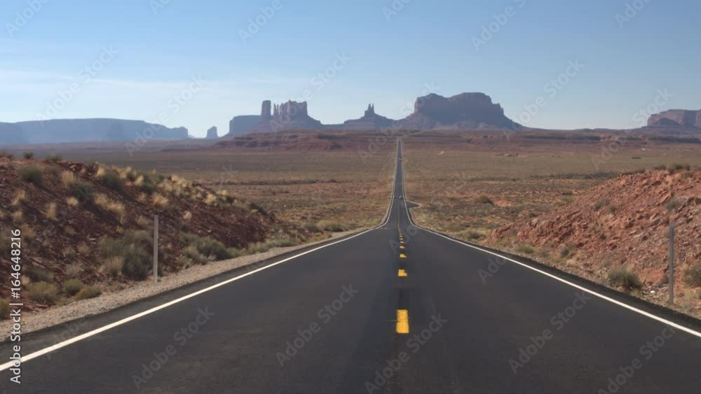 Cars driving along an empty straight road leading towards iconic butte and mesa mountains in Monument Valley, Utah USA. Travelers traveling into stunning desert Monument valley landmark landscape Cars driving along an empty straight road leading towards iconic butte and mesa mountains in Monument Valley, Utah USA. Travelers traveling into stunning desert Monument valley landmark landscape