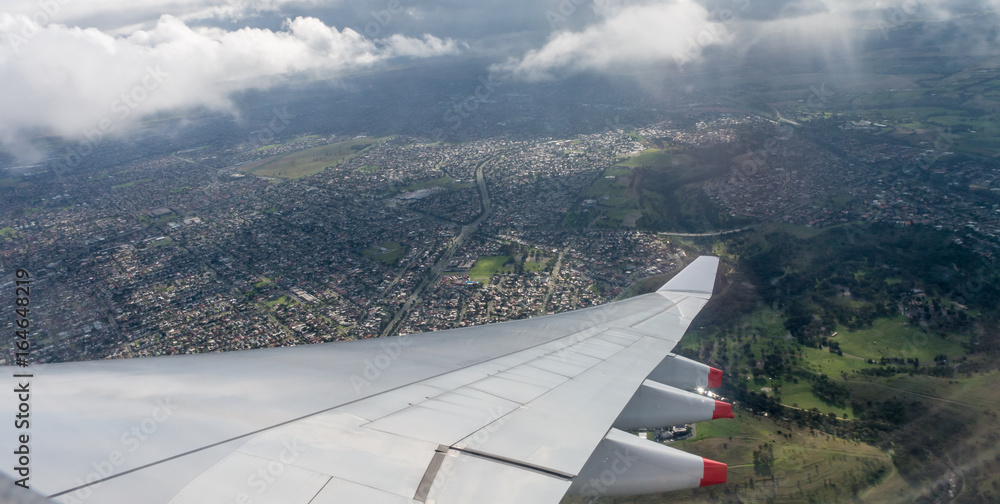 Airplane window view showing wing of plane flying over clouds and over a town