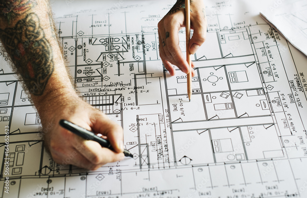 Hands with tattoo working on a blueprint Hands with tattoo working on a blueprint