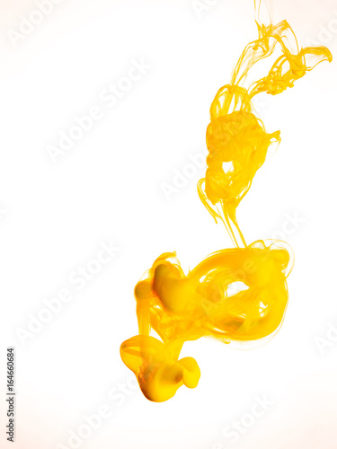 Ink swirl in water isolated on white background. The paint in the water. Soft dissemination a droplets of colored ink in water close-up. Abstract background. Explosion of splashes yellow acrylic ink.